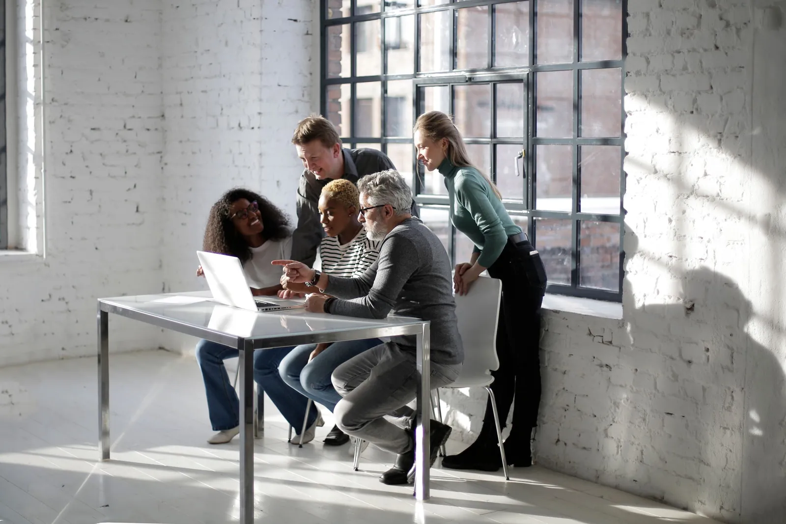 Four colleagues gathered around a laptop at a table in a bright office