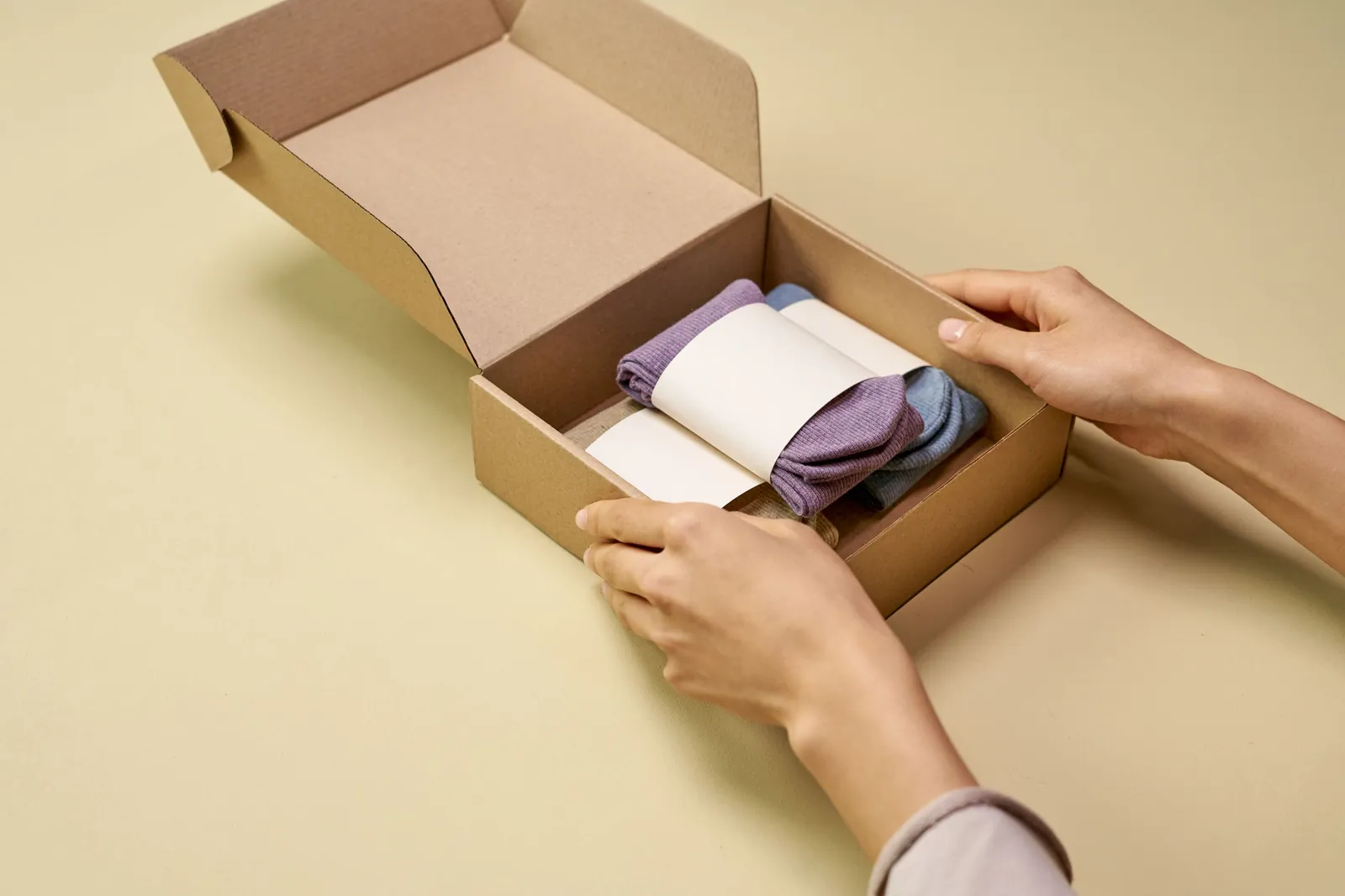 Hands packing folded socks into a small cardboard shipping box