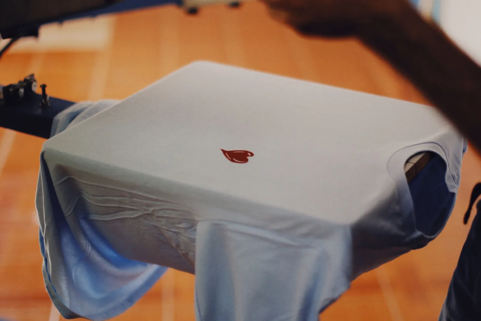 A white t-shirt on a screen printing press, freshly printed with a small logo