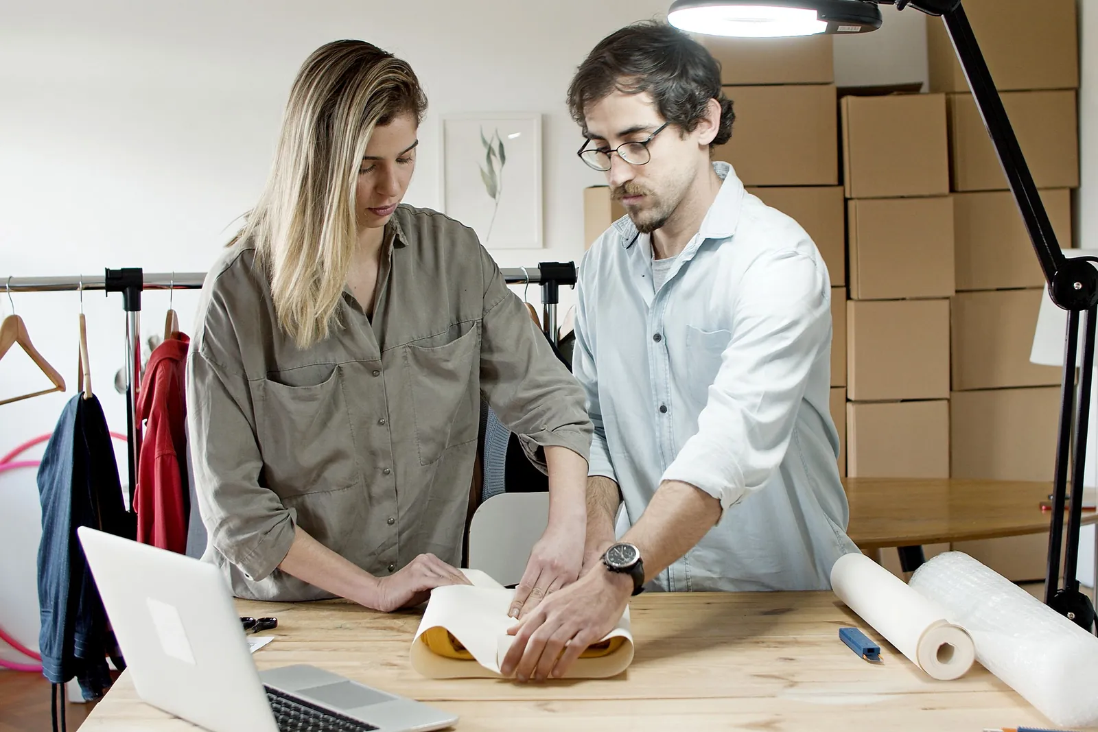 Two people wrapping a garment order for shipping at a workbench with boxes behind them