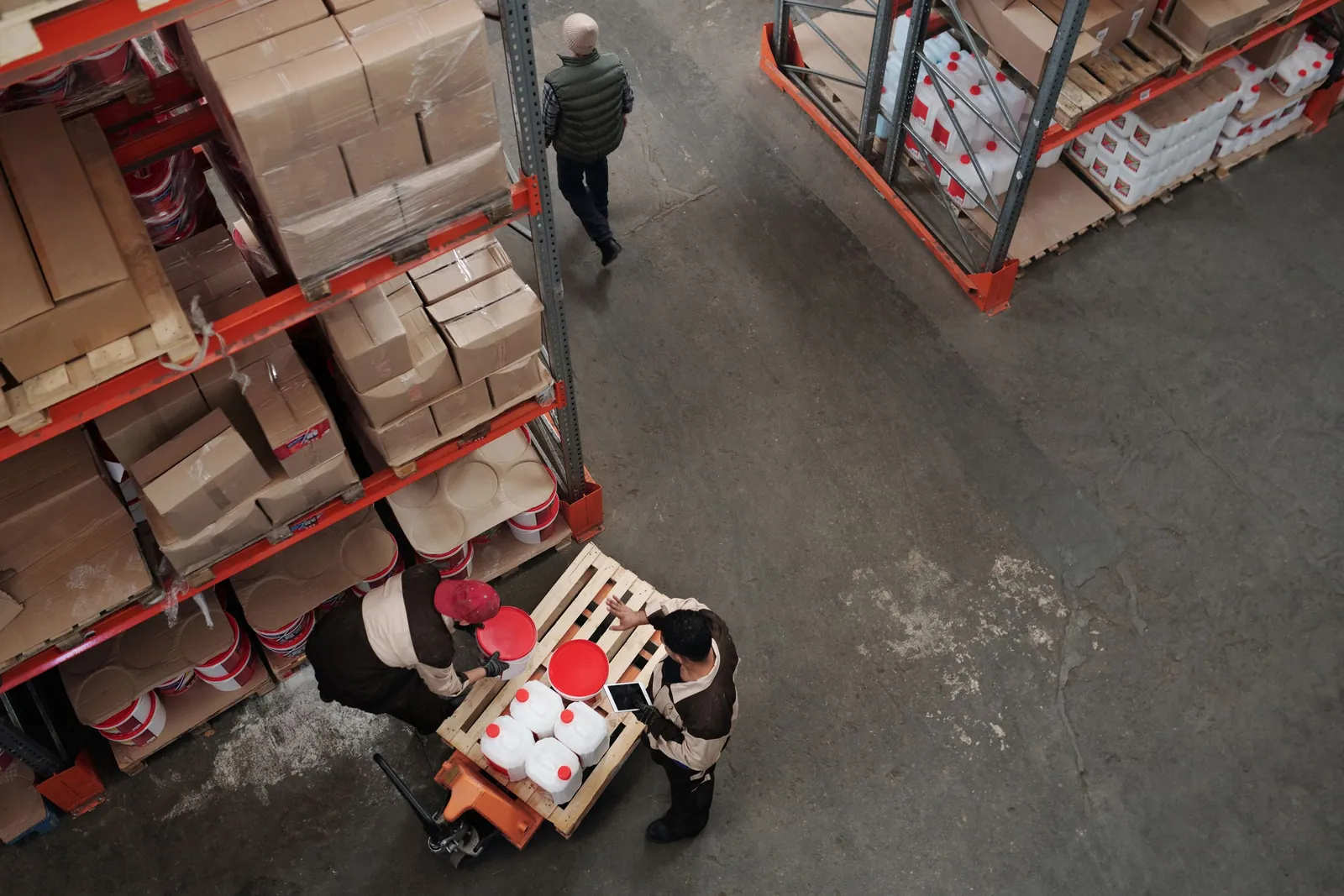 Warehouse workers handling stock on a pallet between shelving racks, seen from above