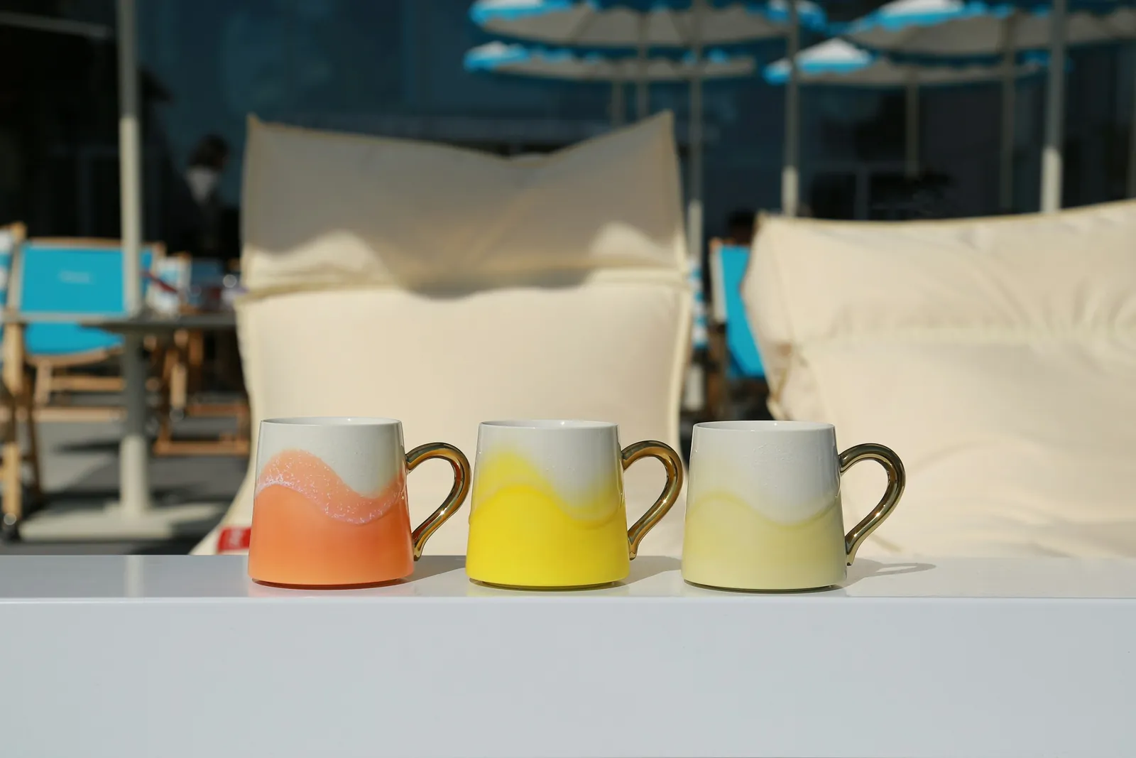 Three ceramic mugs in orange, yellow and cream with gold handles
