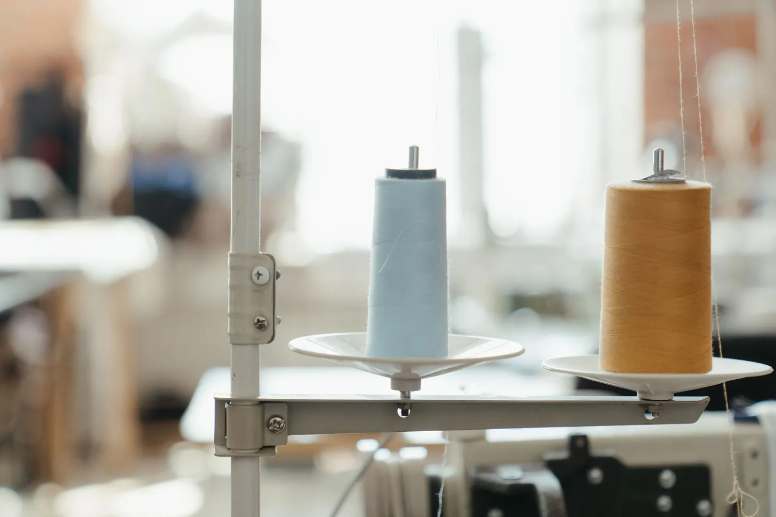 Spools of light blue and tan thread on an industrial sewing machine stand in a sewing workshop