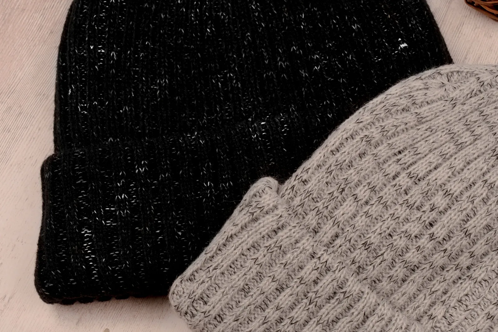 A black knit beanie and a gray cuffed knit beanie lying on a wooden surface