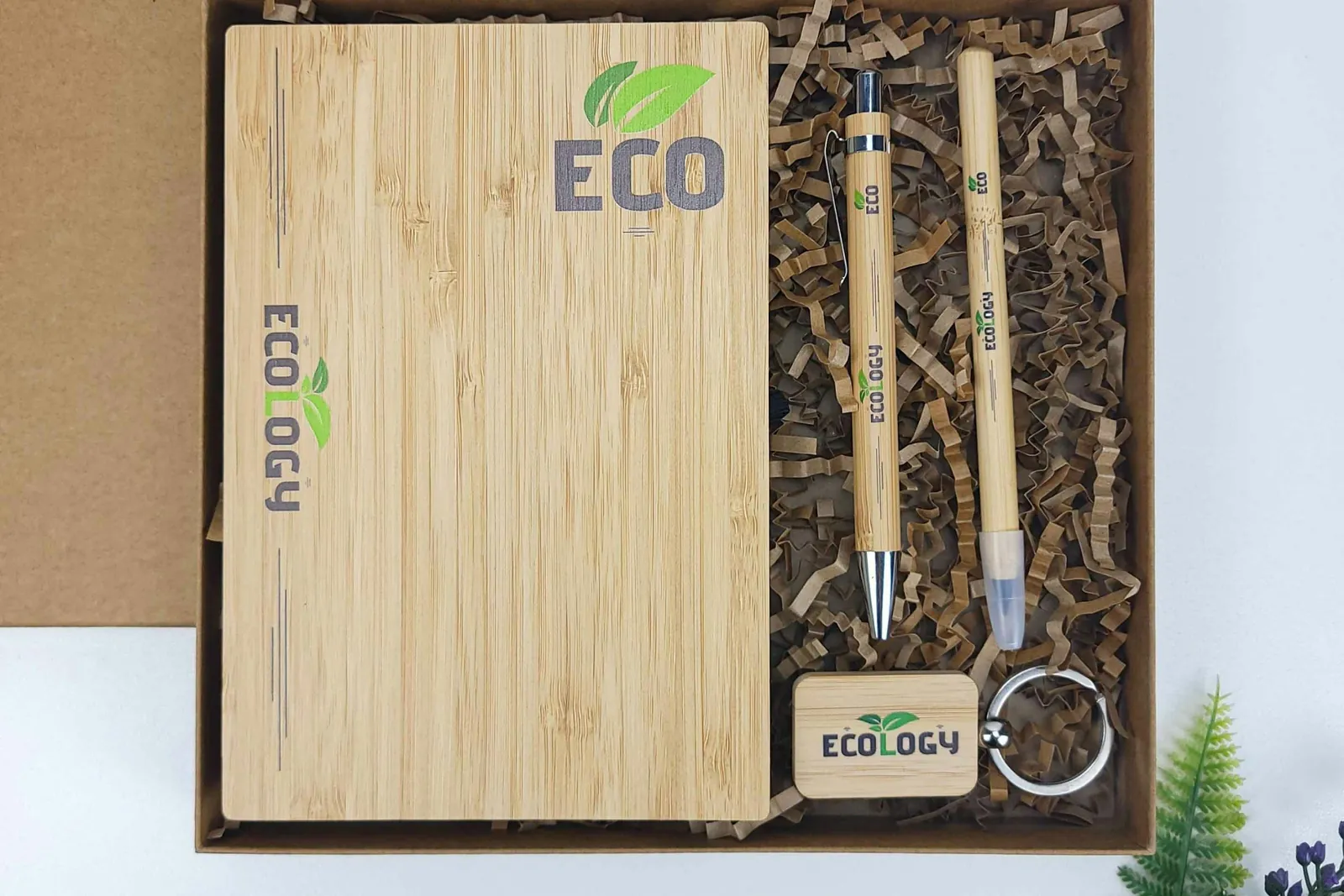 A bamboo notebook, bamboo pens and a wooden keychain in a gift box with paper filler