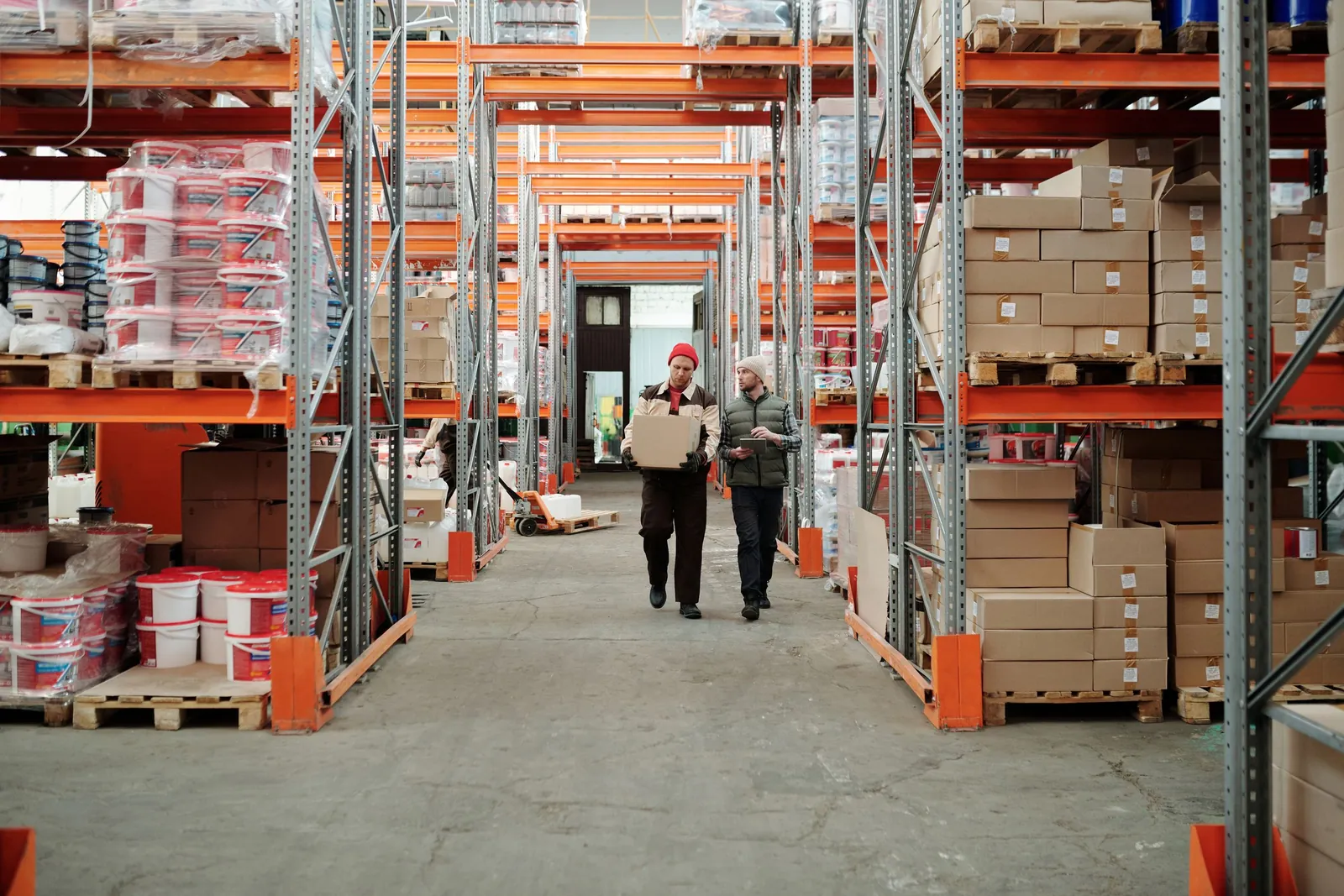 Two workers walking down a warehouse aisle lined with stocked pallet racks
